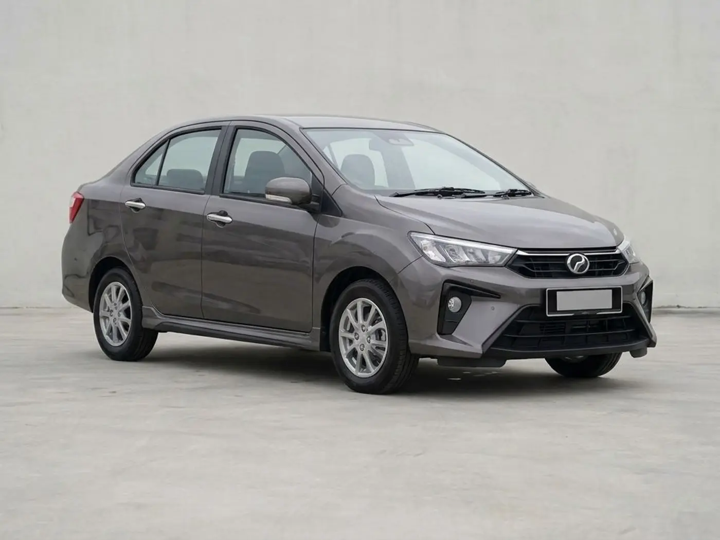 A dark grey Perodua Bezza sedan on a concrete forecourt