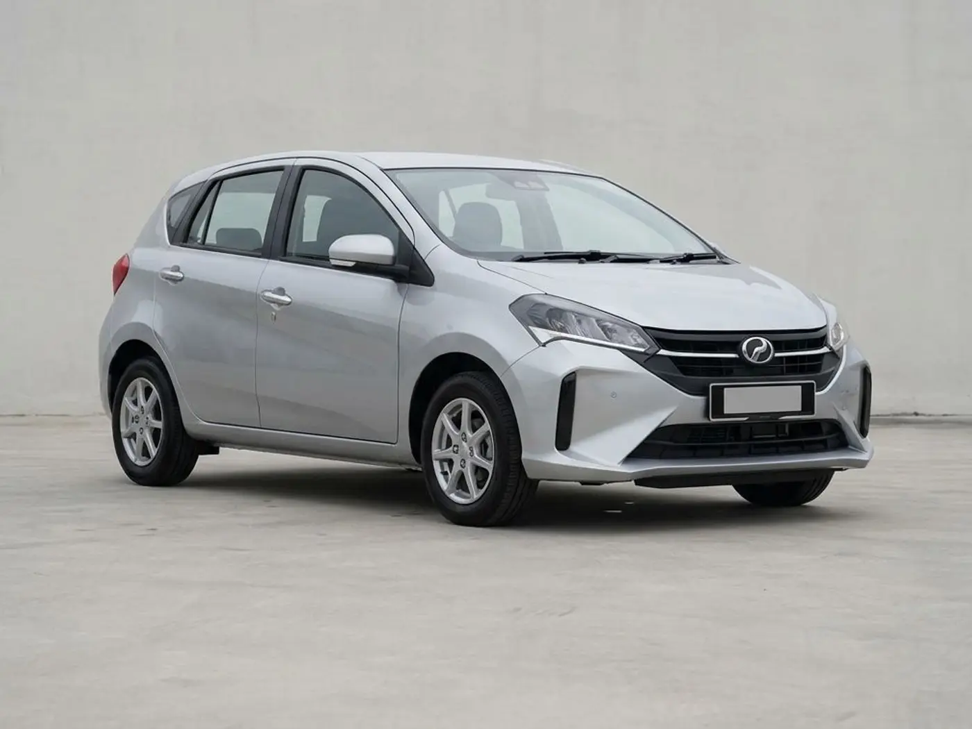A silver Perodua Myvi hatchback on a concrete forecourt